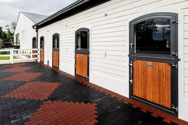 A white barn building with red and black rubber pavers on the ground in an argyle pattern