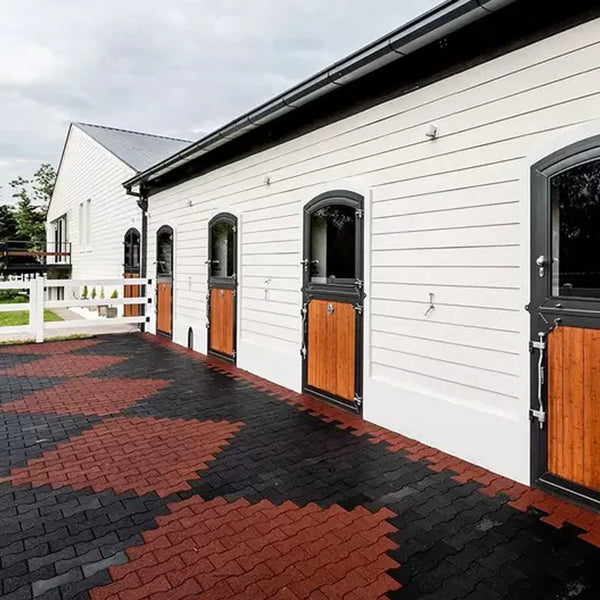 A white barn building with red and black rubber pavers on the ground in an argyle pattern
