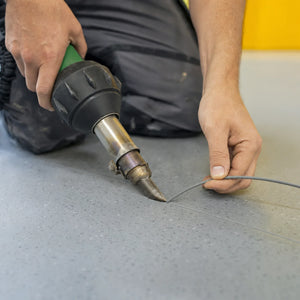 Installer welding ECORE Baller Weld Rod into a routed groove along a vinyl floor seam with a hot-air welder