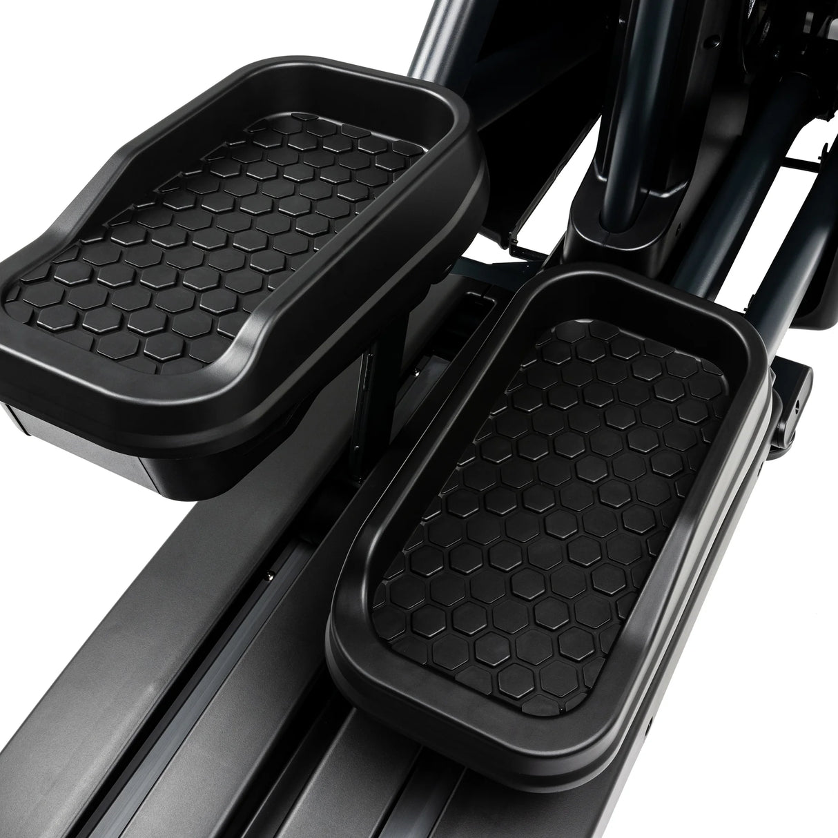 Close-up view of two black, hexagon-patterned foot pedals on the Spirit Fitness CE900 Elliptical by Spirit Fitness, showing surrounding metallic and plastic components.