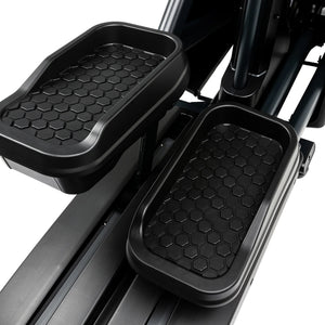 Close-up view of two black, hexagon-patterned foot pedals on the Spirit Fitness CE900 Elliptical by Spirit Fitness, showing surrounding metallic and plastic components.
