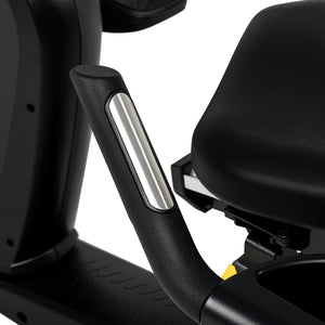 Close-up of the Spirit Fitness CR1000ENT Recumbent Bike's side handgrip with a brushed metal heart-rate contact strip, positioned beside the cushioned seat.