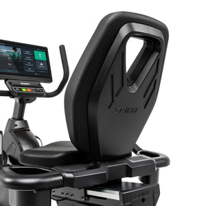 Angled close-up of the Spirit Fitness CR1000ENT Recumbent Bike's backrest showing the embossed Spirit logo and molded carry handle, with the touchscreen console visible in the background.