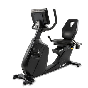 Rear three-quarter view of the Spirit Fitness CR1000ENT Recumbent Bike featuring the back of the touchscreen console, the backrest's molded carry handle, a foot pedal with strap in the foreground, and the Spirit logo on the base rail.