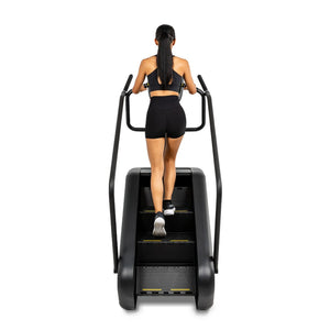 Rear view of a woman climbing the Spirit Fitness CSC880 Stair Climber using the dual side handrails.