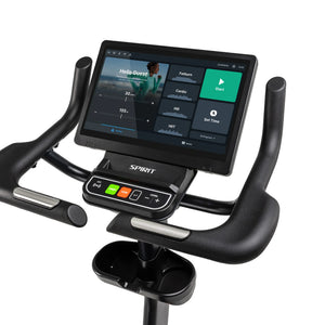 Close-up angled view of the Spirit Fitness CU1000ENT Upright Bike console displaying the training menu, with the physical NFC, Start, Stop, and Level control panel and dual accessory tray visible below the screen.